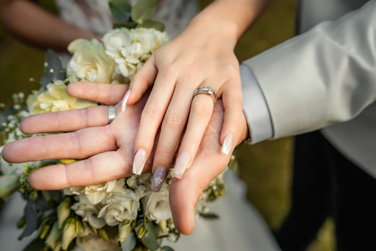 A bride and groom's hands holding a bouquet of flowers.