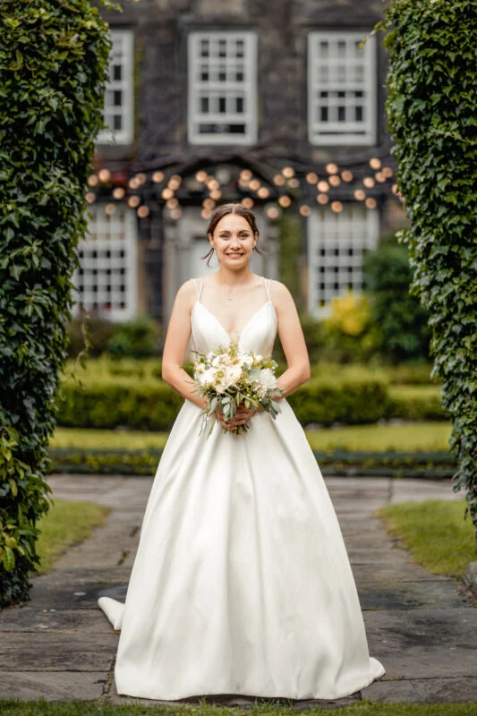A bride in a white dress standing in front of a mansion.