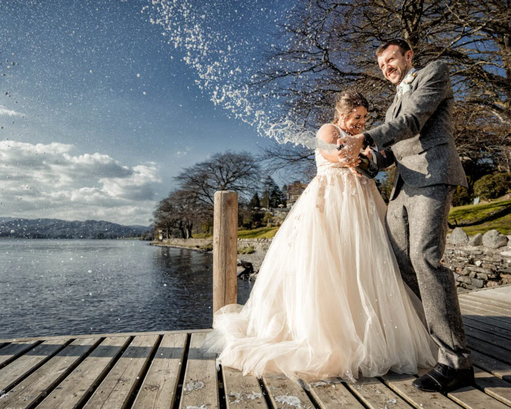 A bride and groom standing on a dock with water sprayed on them.