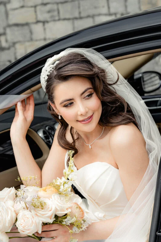 A bride in a wedding dress sitting in a car.