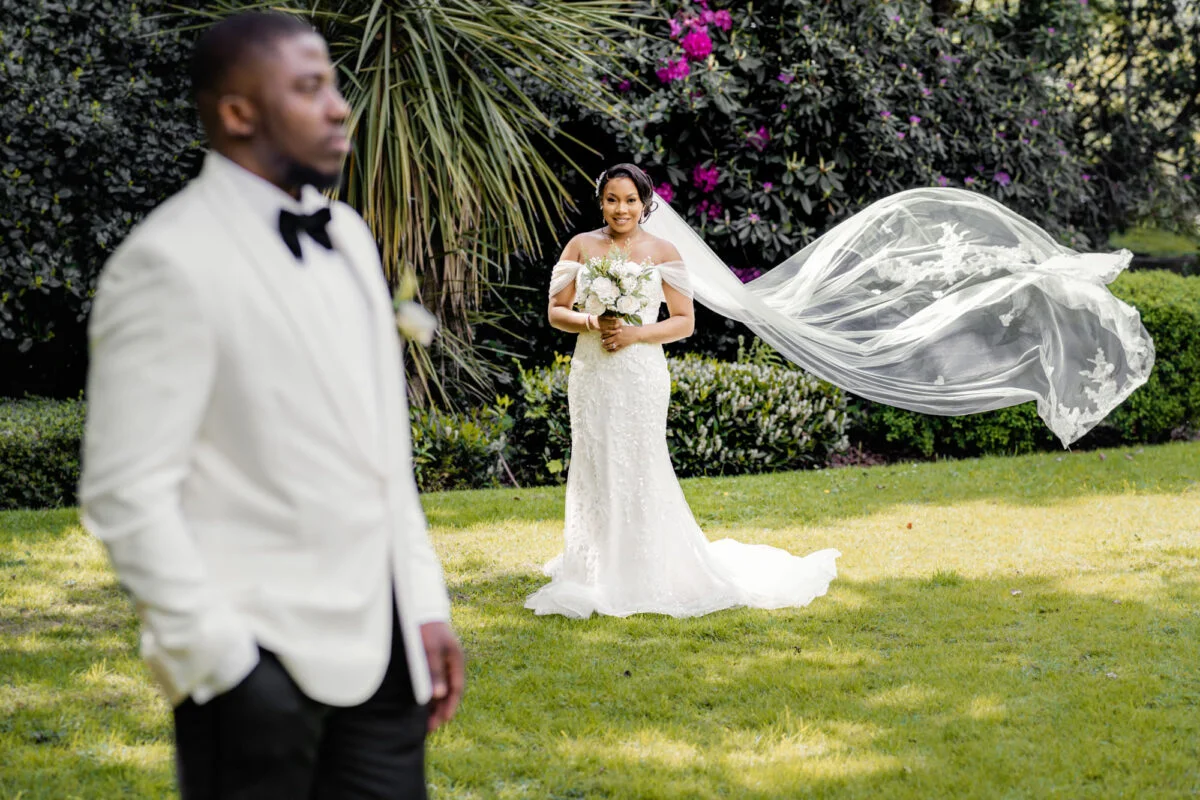 A bride and groom in a white tuxedo standing in a garden.