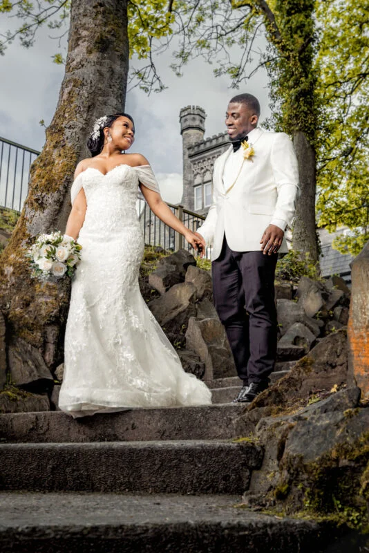 A bride and groom walking down steps in front of a castle.