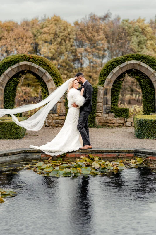 A bride and groom kissing in front of a pond.