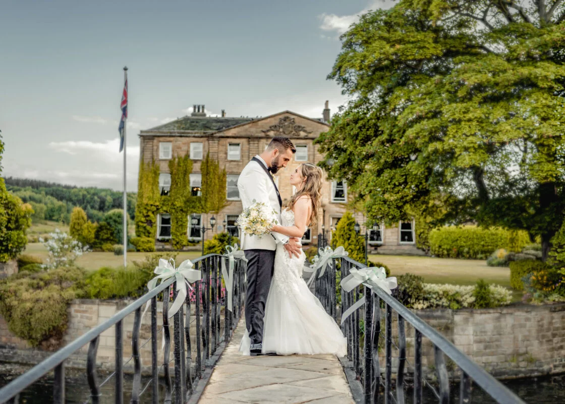 A bride and groom kissing on a bridge in front of a large mansion.