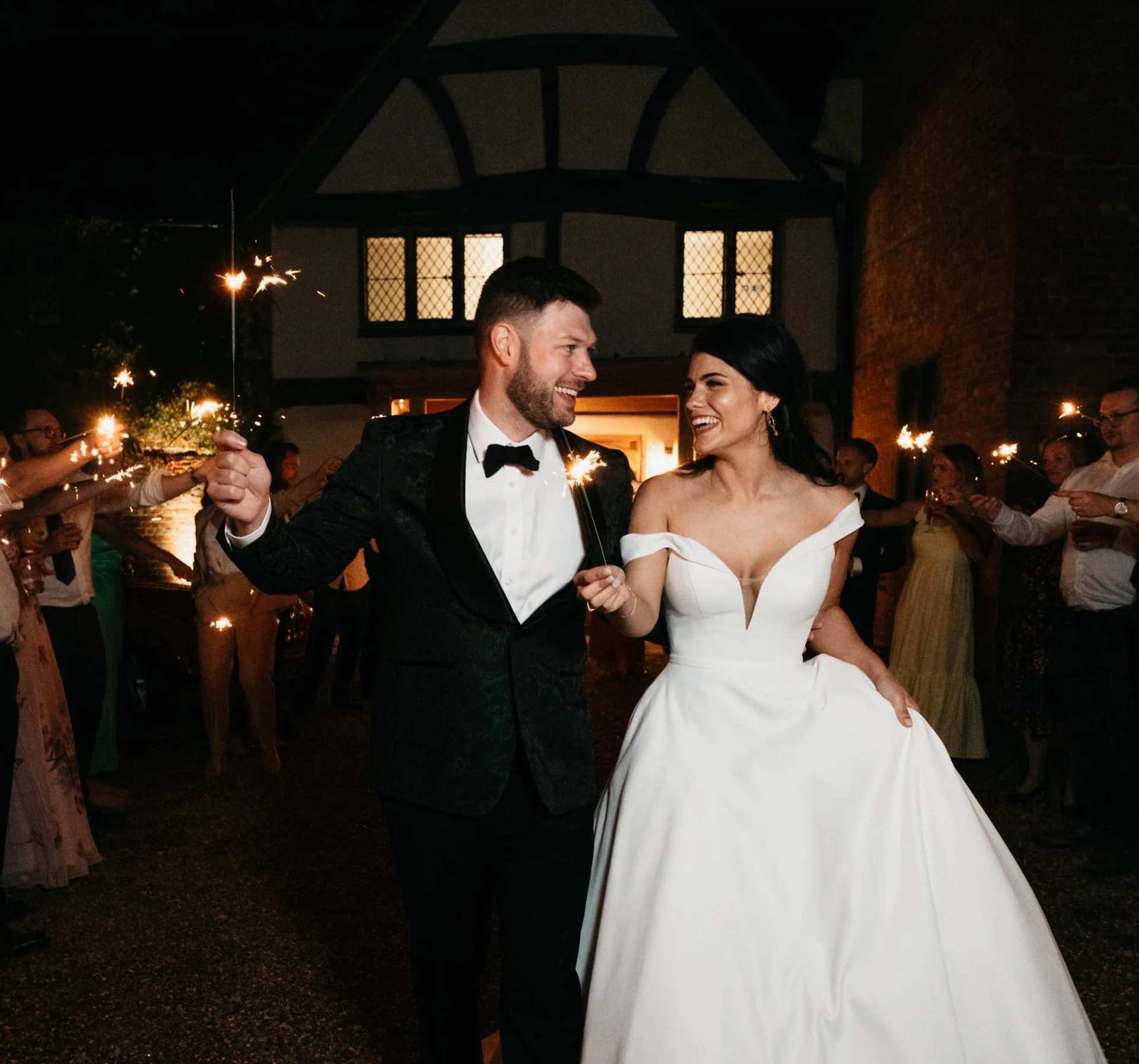 Fairytale wedding photography featuring a bride and groom walking with sparklers in front of a house at night. (listing)