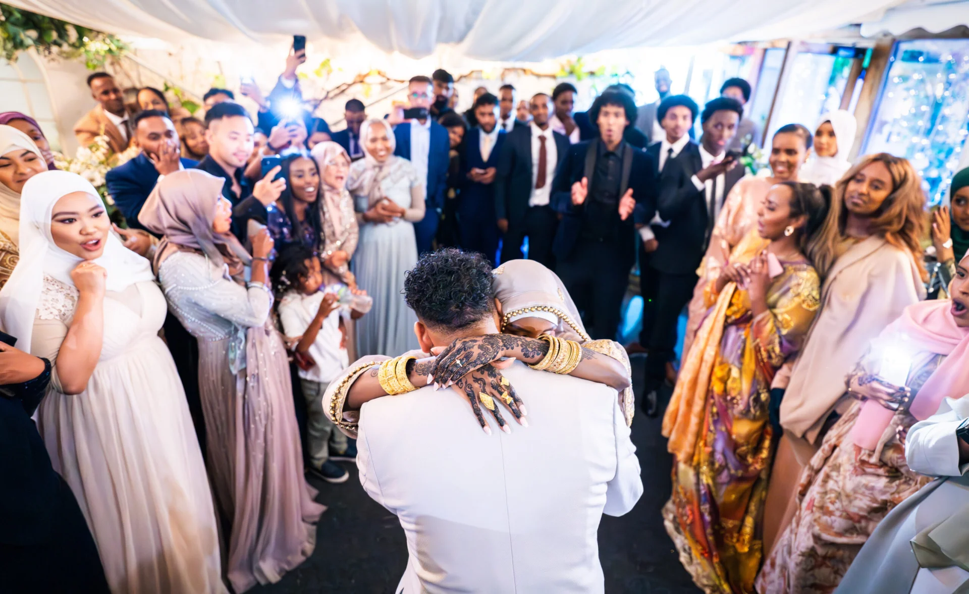 A fairytale bride and groom hugging in front of a crowd of people captured by wedding photography. (listing)