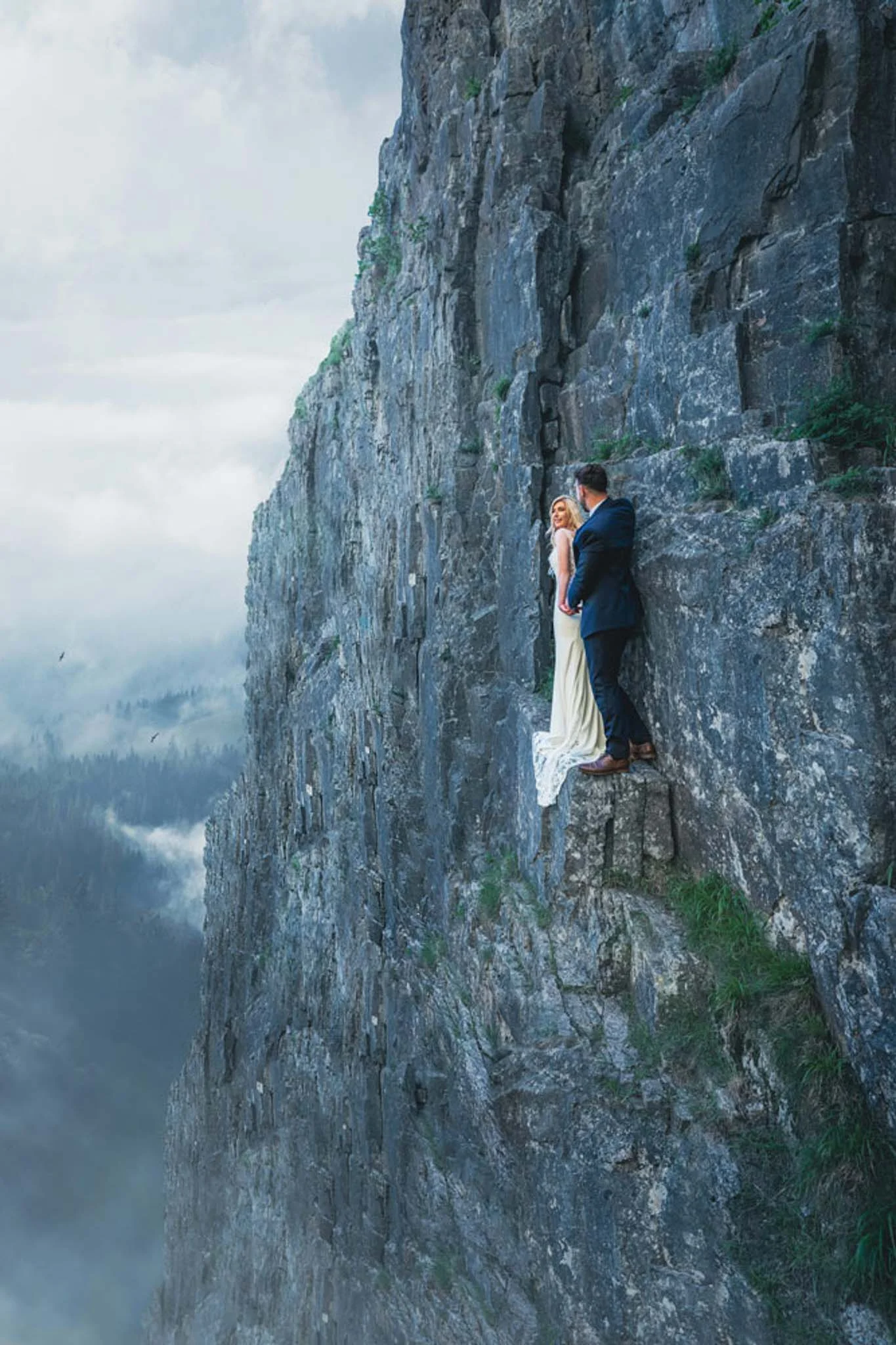Fairytale wedding couple kissing on a cliff edge. (listing)
