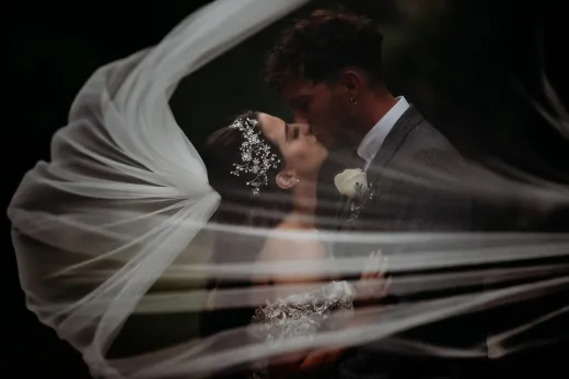 A bride and groom share a kiss under a veil, captured by a London-based wedding photographer.