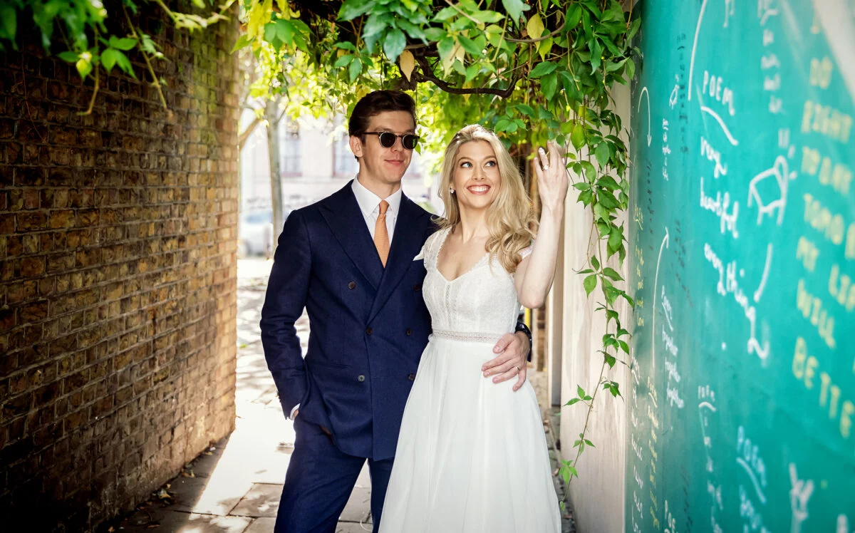 A bride and groom posing in front of a green wall.