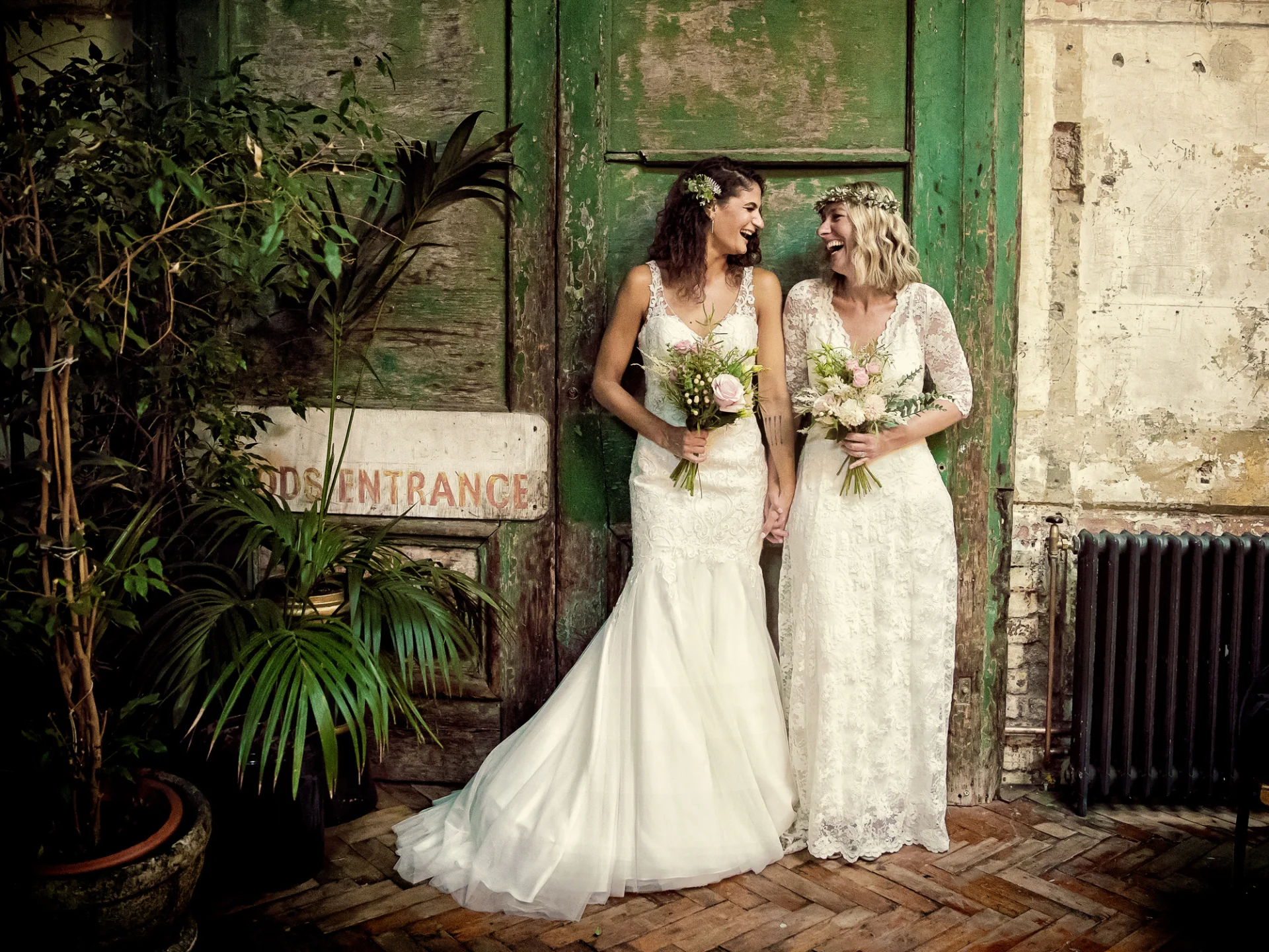 Wedding photographer duo captures two brides in front of a green door. (listing)