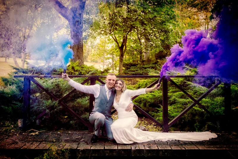 A bride and groom posing with smoke bombs on a bridge.