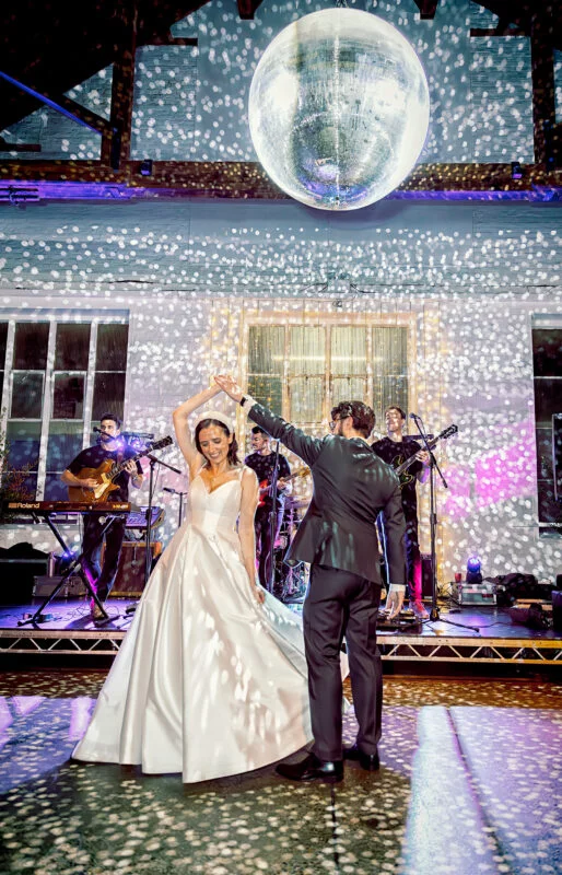 A bride and groom dancing in front of a disco ball.