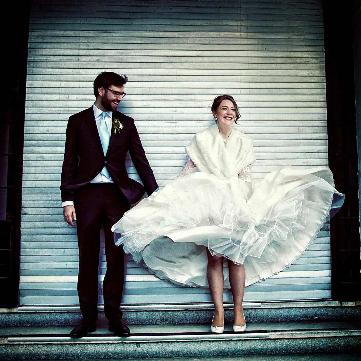 A wedding photographer duo capturing a bride and groom posing in front of a door. (listing)