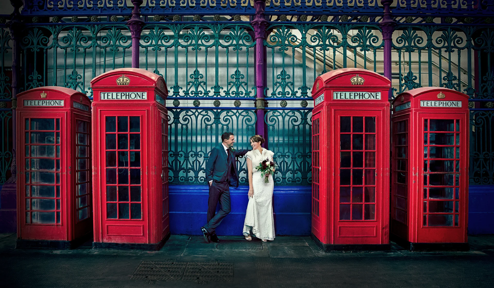 A wedding photographer duo capturing a bride and groom in front of telephone booths. (listing)