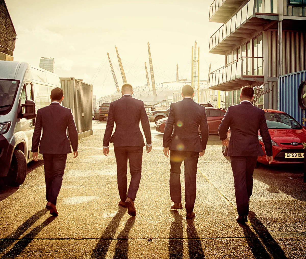A duo of wedding photographers capturing men in suits walking in a parking lot. (listing)