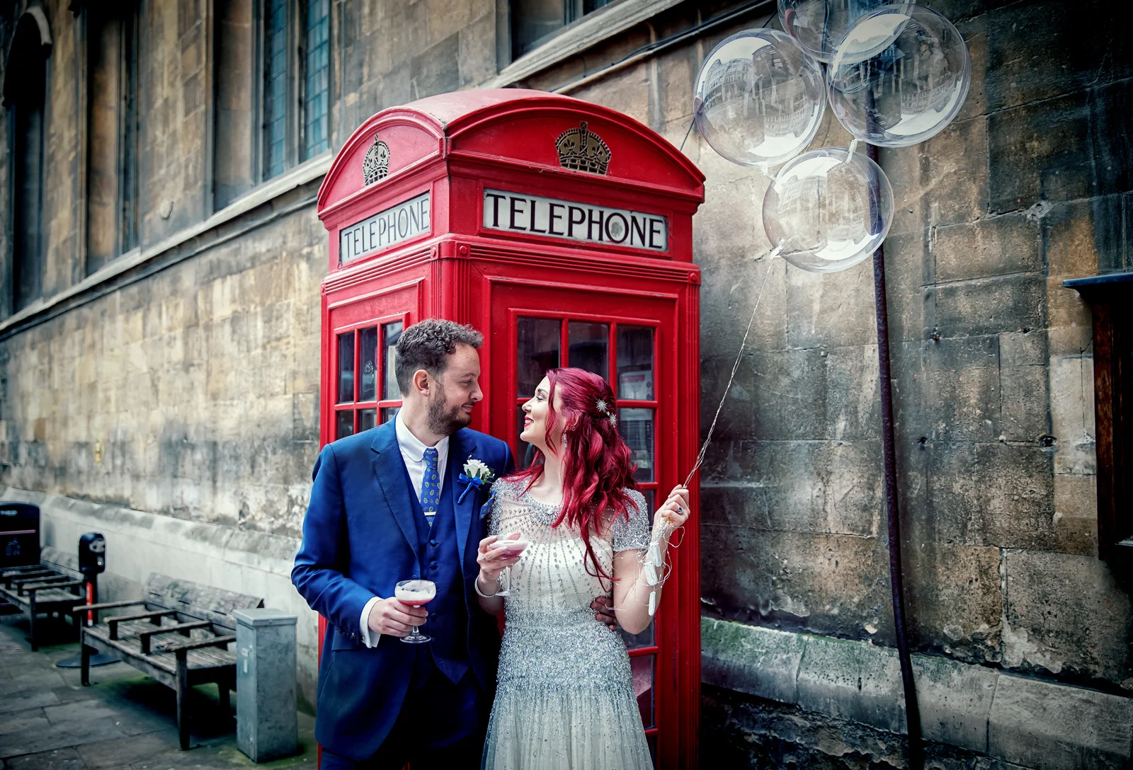 A wedding photographer duo captures a bride and groom in front of a telephone booth. (listing)