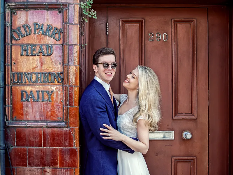 A wedding photographer duo capturing a bride and groom posing in front of a door. (listing)
