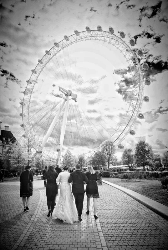 A black and white photo of a wedding party walking in front of the london eye.