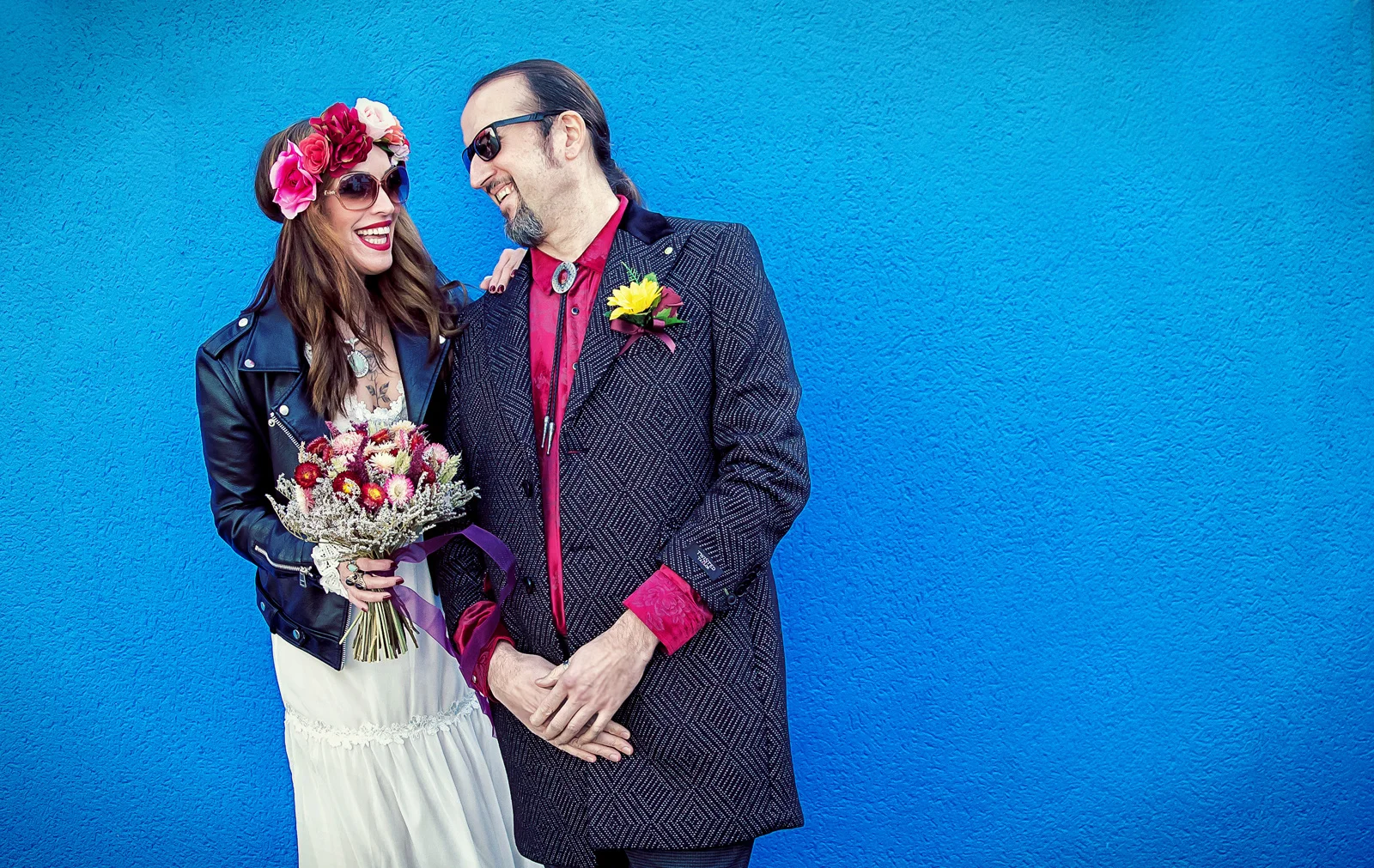 A Wedding photographer duo capturing a bride and groom in front of a blue wall. (listing)