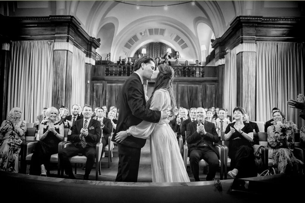 A bride and groom kiss in front of a crowd of people.