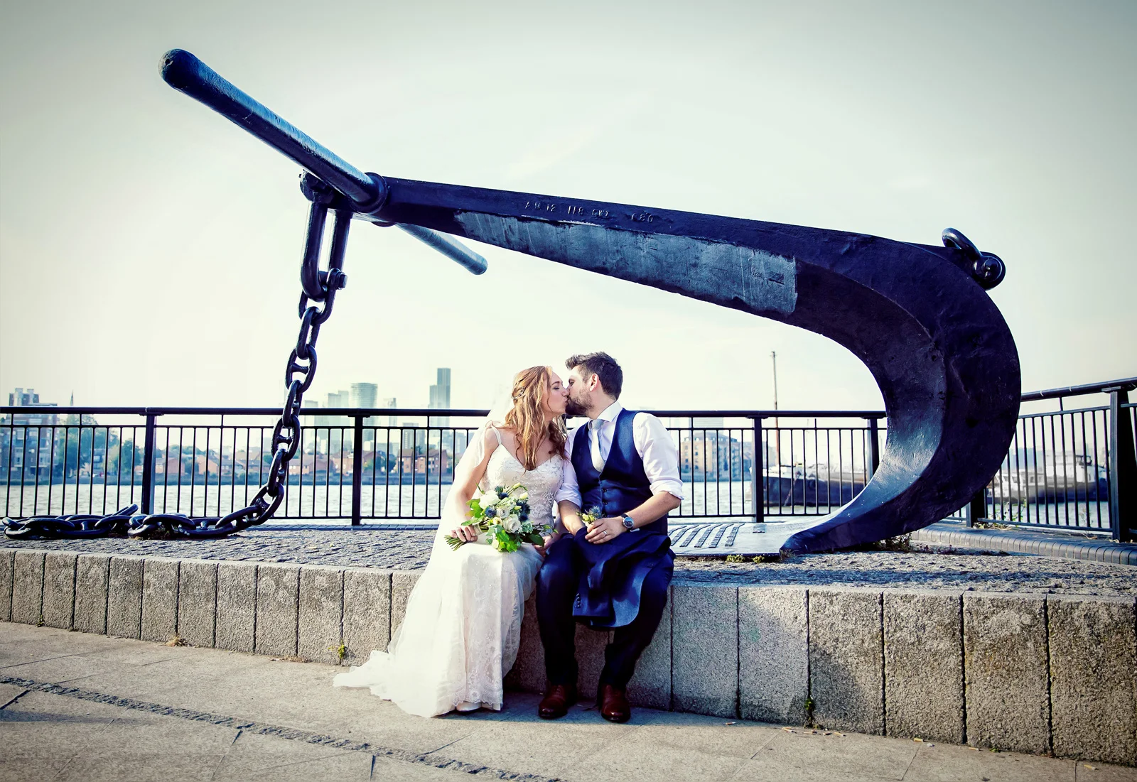 A wedding photographer duo captures a bride and groom kissing in front of a large metal sculpture. (listing)