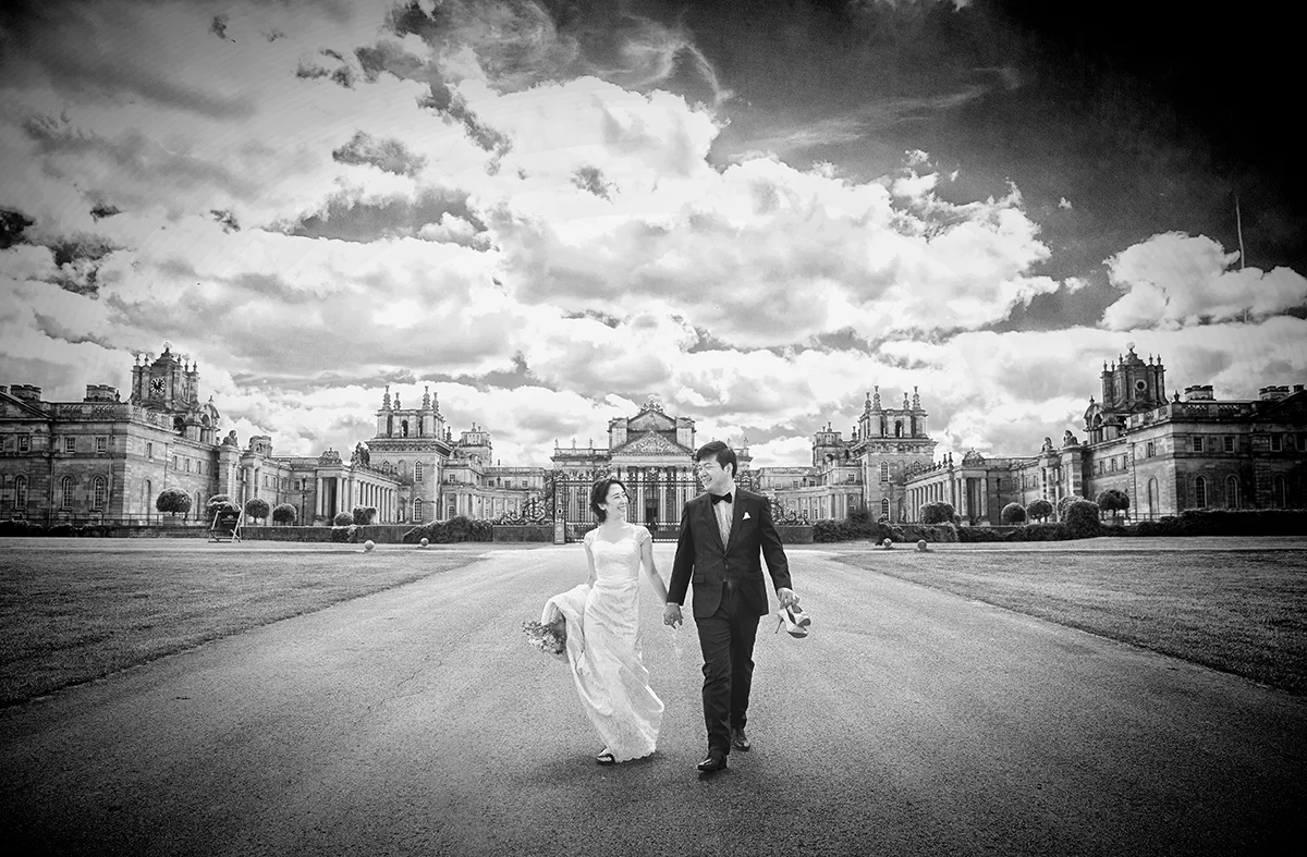 A wedding photographer duo capturing a bride and groom in front of a large building. (listing)