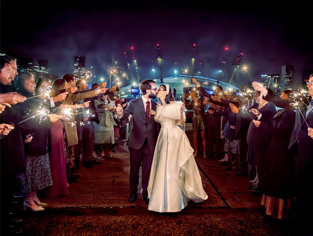 A bride and groom holding sparklers in front of a crowd.