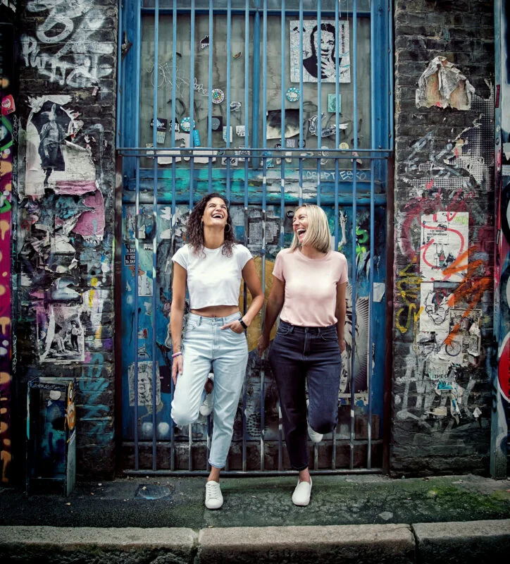 Two women standing in front of a graffiti covered wall.