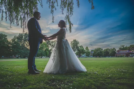 A bride and groom standing under a willow tree at sunset.
