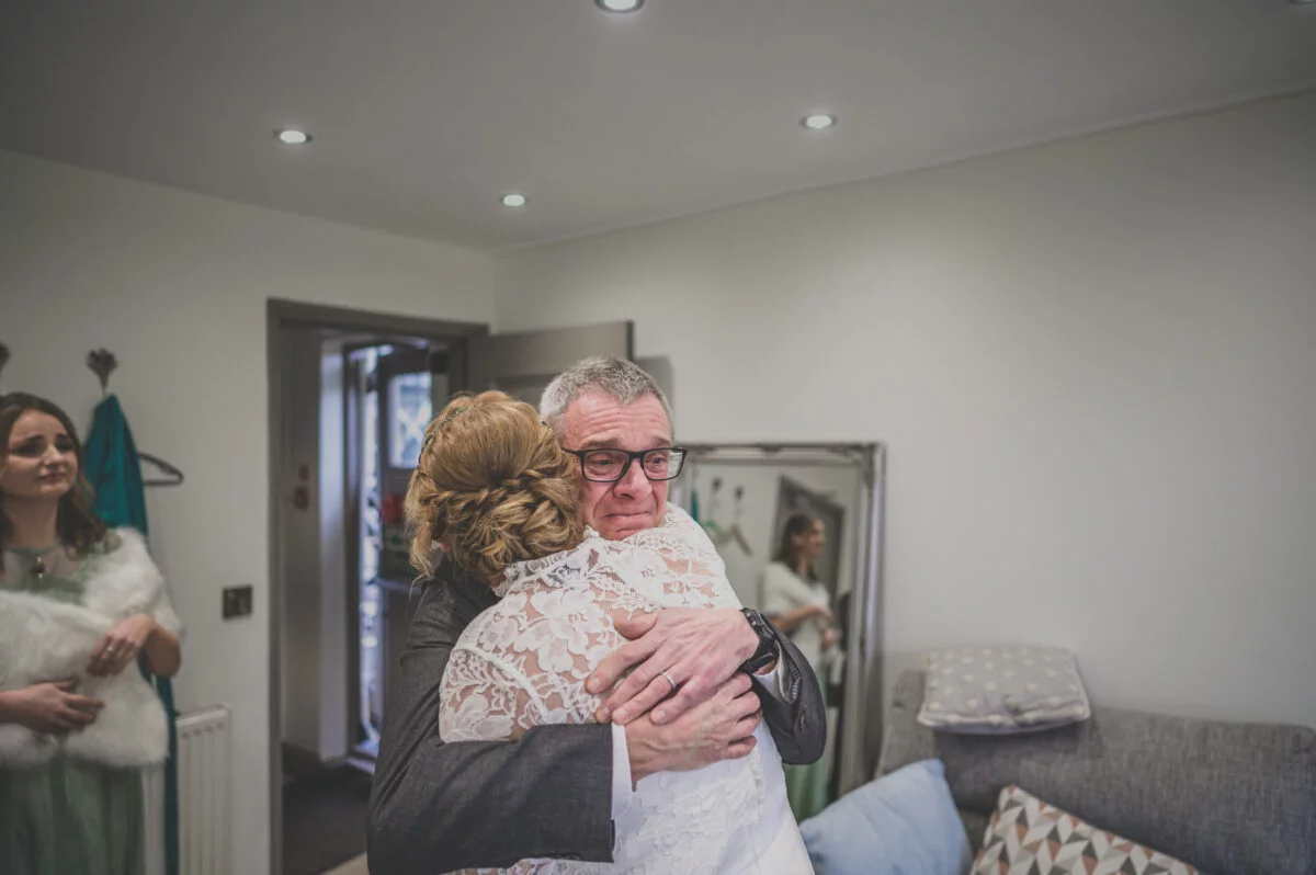 A bride is hugging her father in front of a mirror.