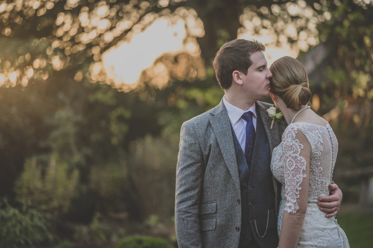 A bride and groom kissing in the garden at sunset.