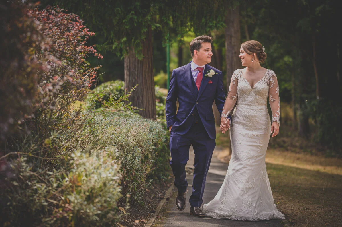 A bride and groom walking down a path in a park.