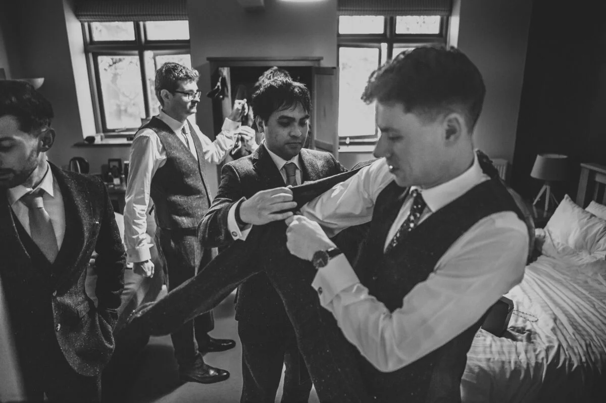 A black and white photo of a group of men getting ready for a wedding.