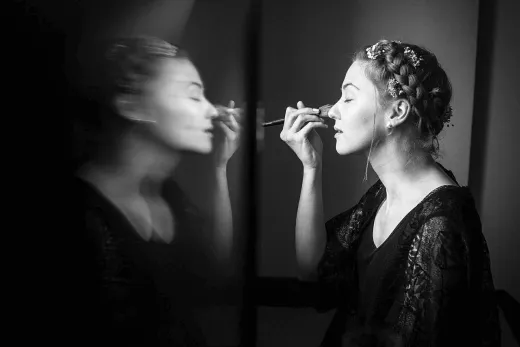 A woman is getting her makeup done in a mirror.
