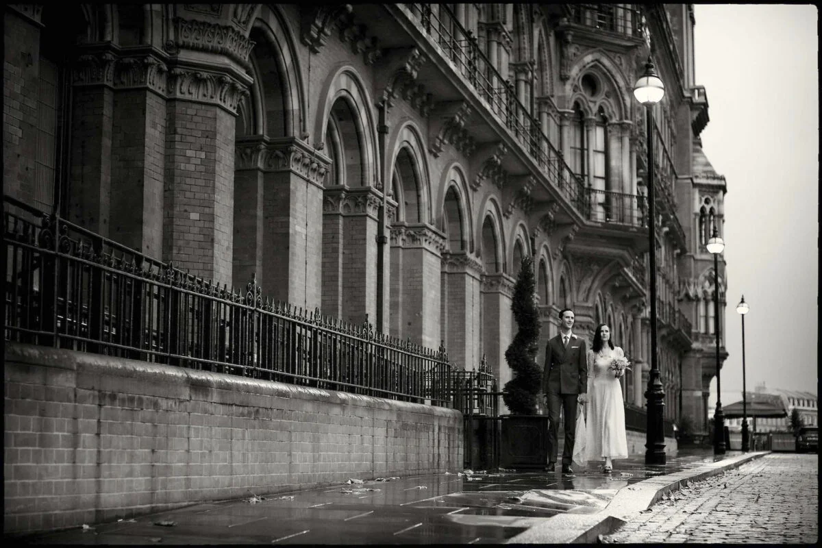 A bride and groom standing on a wet street.