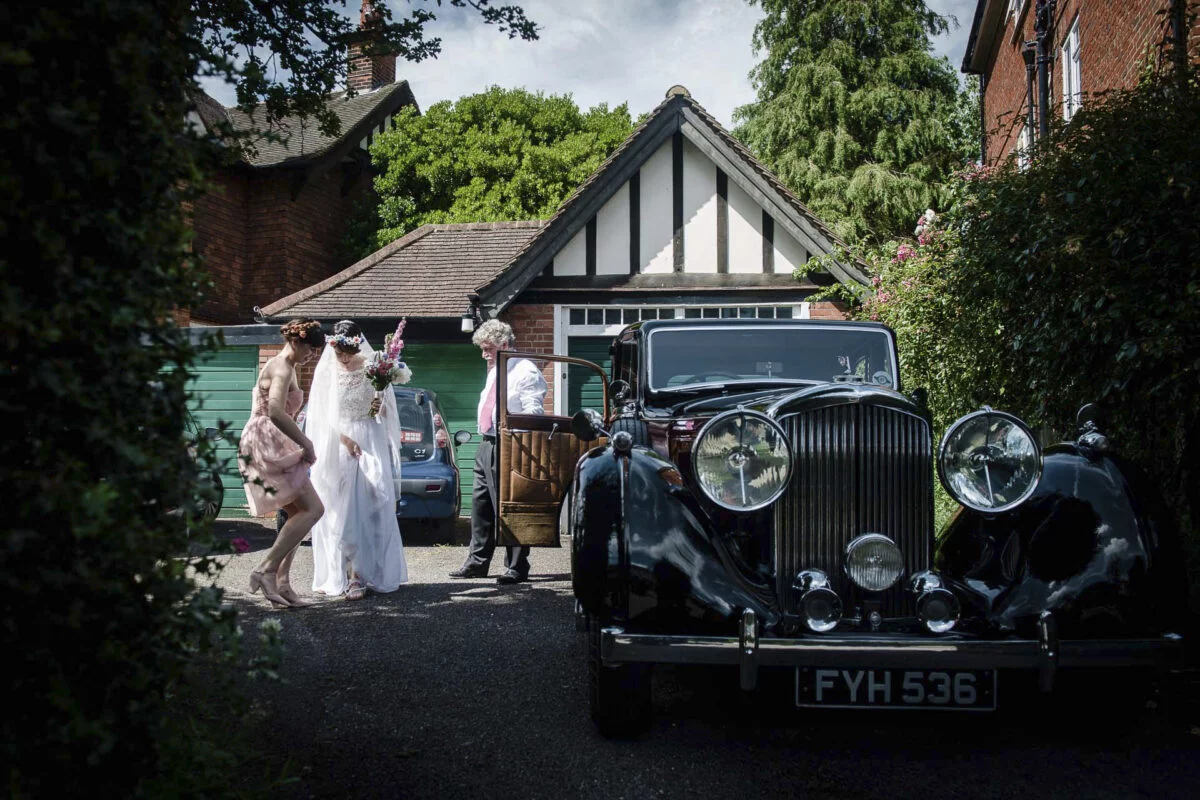 A bride and groom standing next to a vintage car.