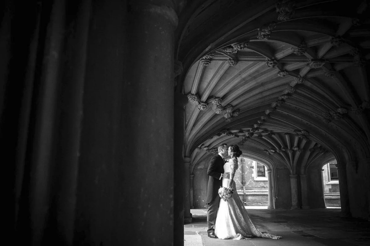 A bride and groom standing under arches in a black and white photo.