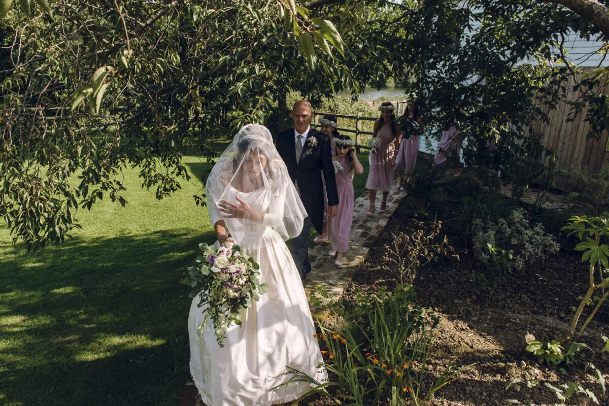 A bride and her bridesmaids walk through a garden.