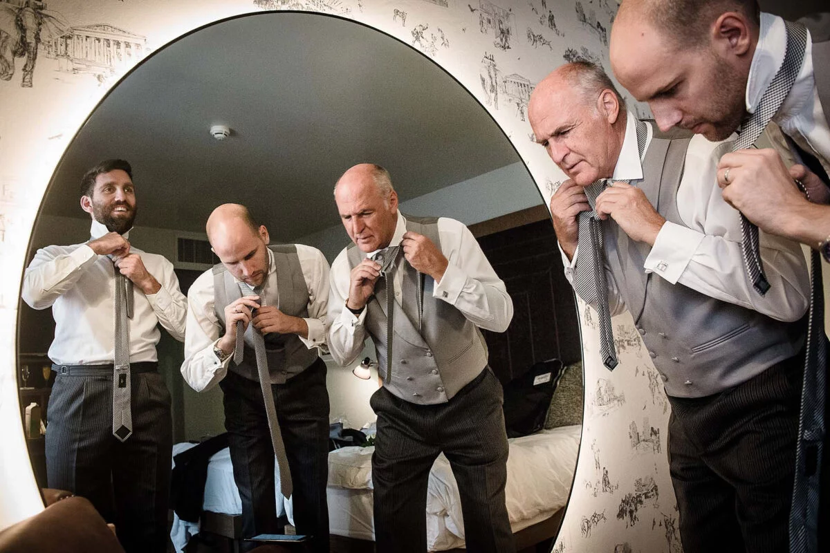 A group of men are adjusting their ties in front of a mirror.