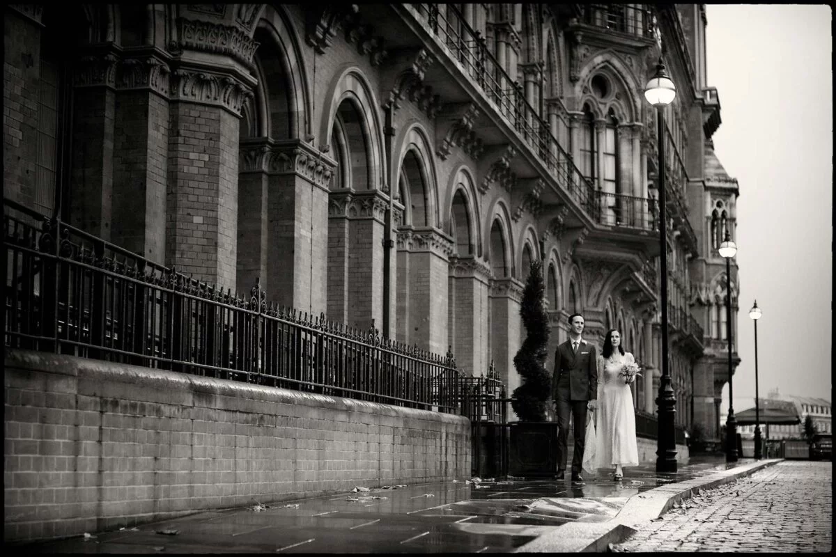 A bride and groom standing on a wet street.