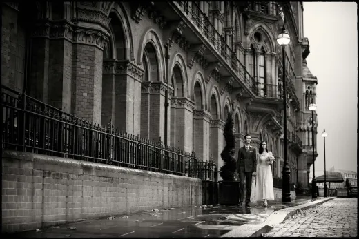 A bride and groom standing on a wet street.