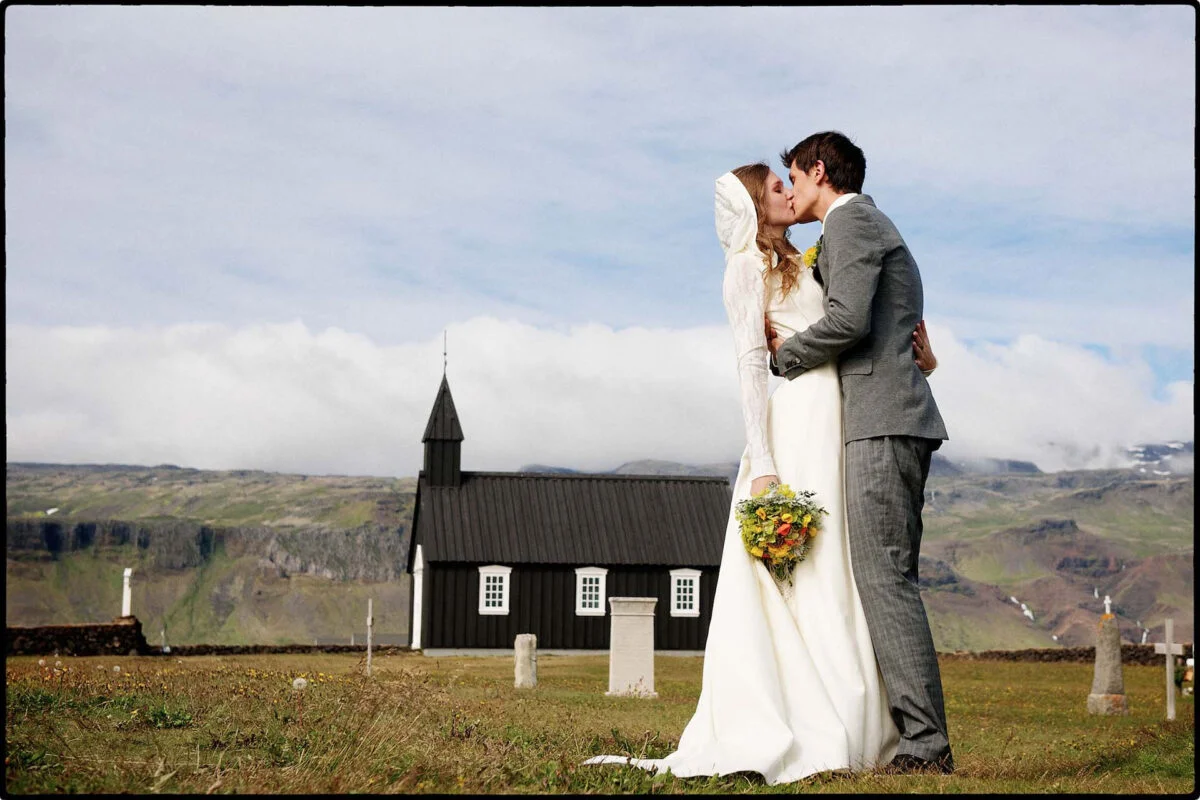 A bride and groom kiss in front of a church in iceland.