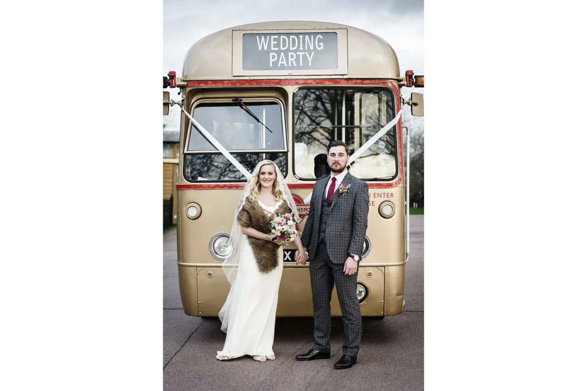 A bride and groom standing next to a vintage double decker bus.