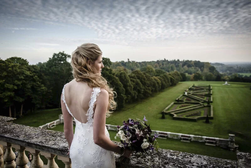 A bride in a wedding dress standing on a balcony overlooking a field.
