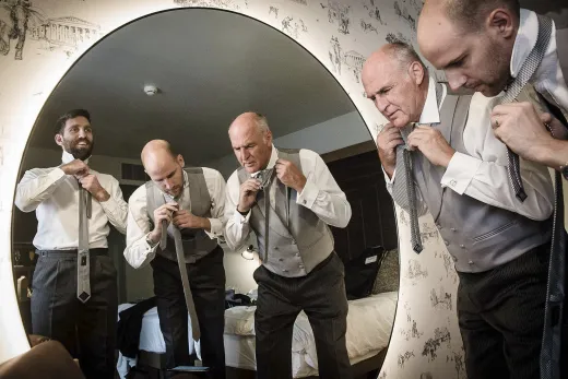 A group of men adjusting their ties in front of a mirror.