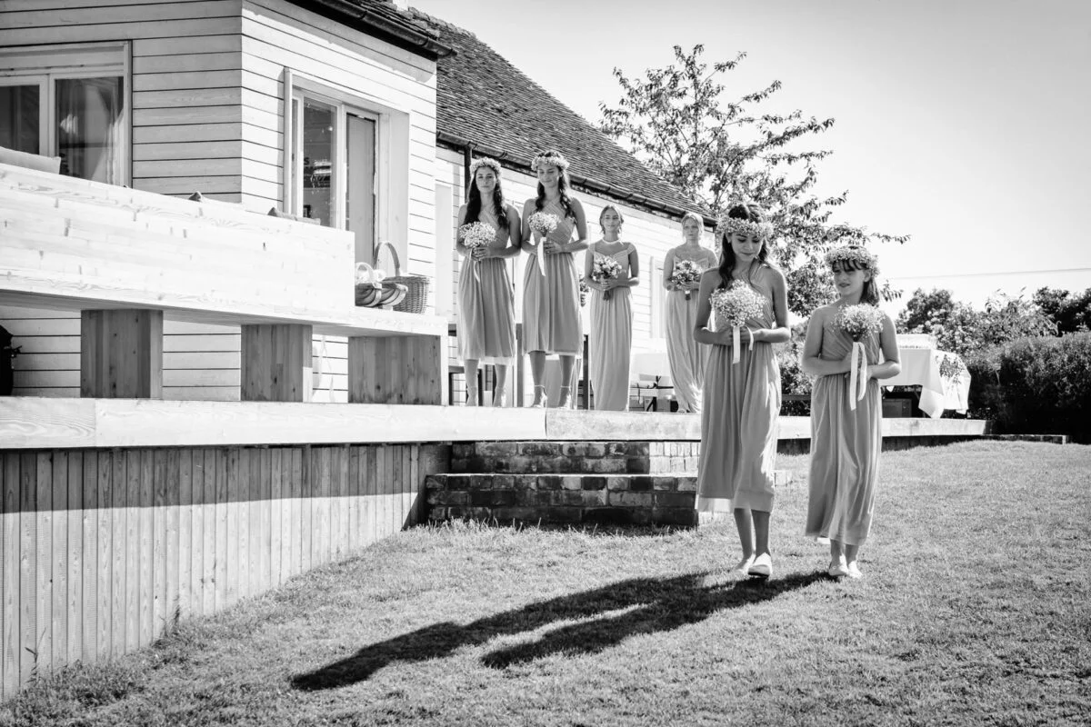 Black and white photo of bridesmaids walking in front of a house.