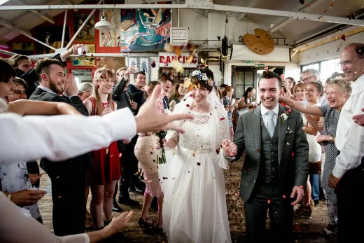 A bride and groom walk down the aisle with confetti thrown at them.
