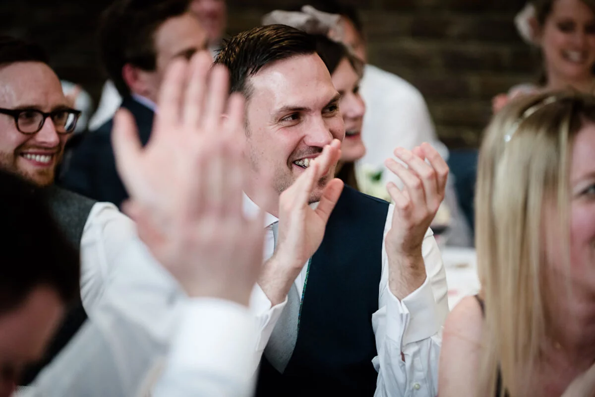 Wedding guests laughing and applauding enthusiastically during the reception speeches.