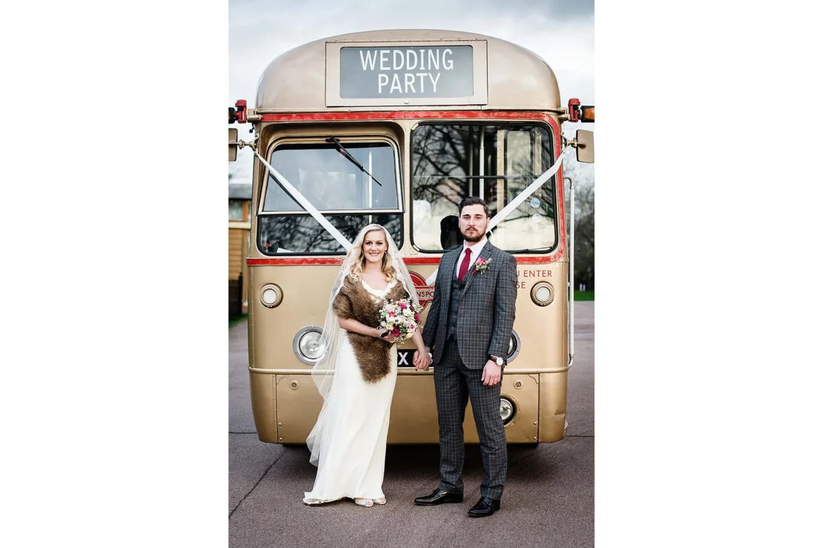 A bride and groom standing next to a vintage double decker bus.