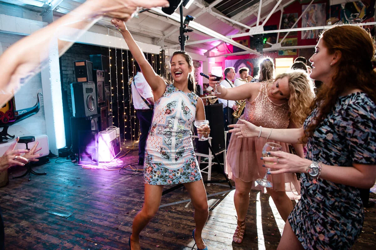 Guests enjoy a lively moment on the dance floor in an industrial warehouse venue with exposed rafters and colourful lighting.